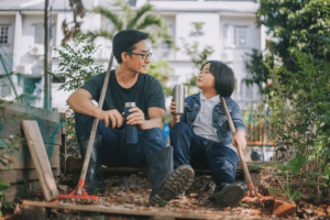 Asian chinese father daughter resting after gardening sitting drinking coffee talking bonding time at backyard vegetable garden.